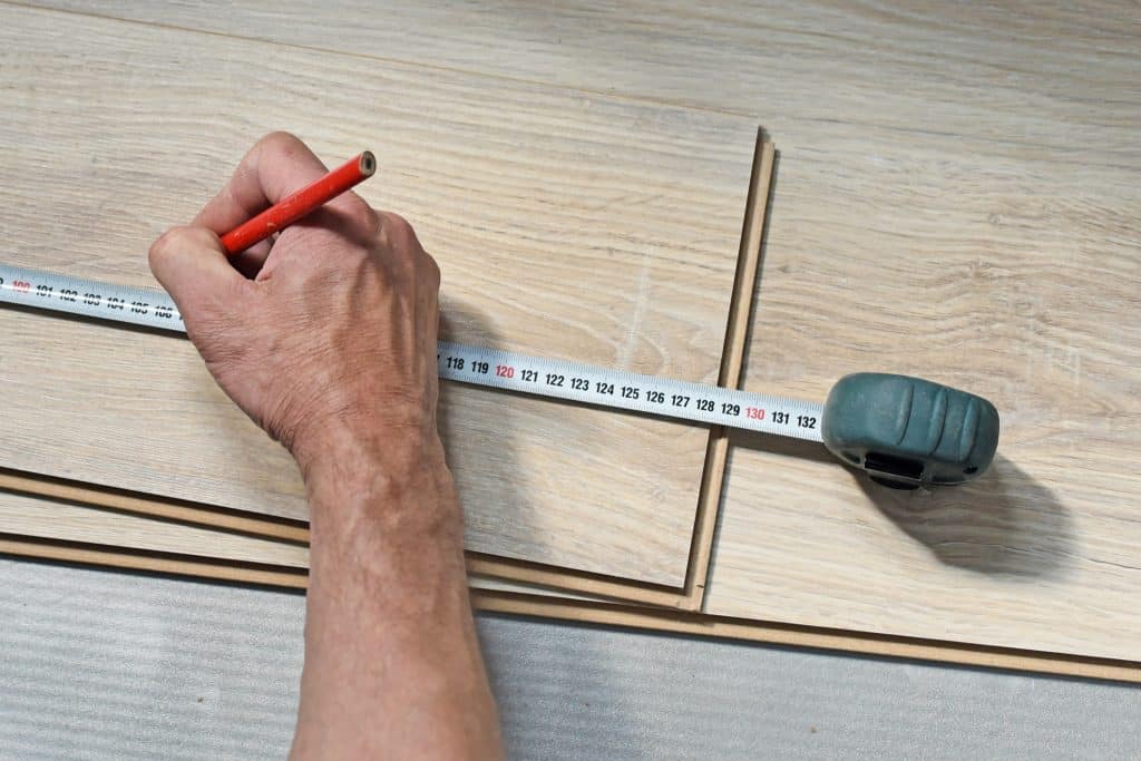 Eine Person misst etwas auf einer Holzplatte aus und markiert sich eine Stelle mit einem roten Bleistift.