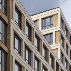 Nahaufnahme eines modernen Bürogebäudes mit einer Fassade aus weißen Steinrahmen, beigefarbenen Akzenten und großen Glasfenstern.