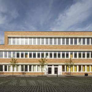 Backsteingebäude mit weißen Fenstern und einem Innenhof mit kleinen Bäumen.